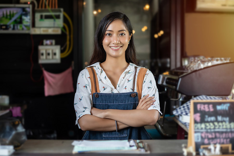 Business Insurance - Women Barista Smiling and Using Coffee Machine in a Coffee Shop from behind the Counter
